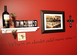 A wall decal on the red colored wall with a photo frames and wines on the display shelf - When in doubt add more wine