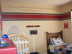 Train up a child on the way he should go and when he is old, he will not depart from it, a wall decal on the center of the wall above the red and blue wallpaper partition, with crib and bed in the Aviation themed boy's room