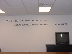 A motivational wall decal in the board room with a table and a television - We improve communication and vocational independence... for life!