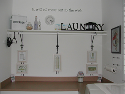 A wall decal on the center of the laundry room with an accessory shelf below - It will all come out to the wash