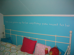 A wall lettering in the boys attic room with a bed and throw pillows in it