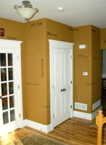 Wall words in different languages in the entrance hall with 2 doors showing and a chandelier on the center